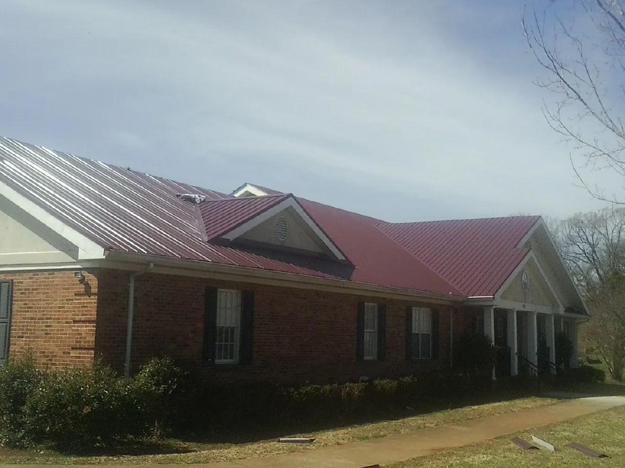 Red metal roof with gabled entries on a long brick building, from a Hail Damage Roof Repair job in Quakertown