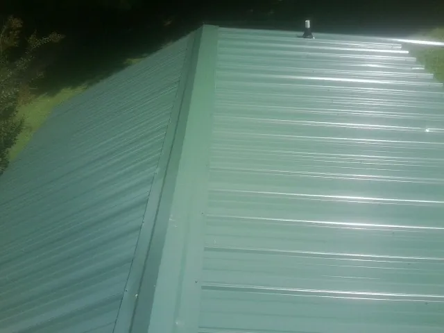 New green metal panels meeting at the ridge of a roof — Flat Roof Repair work by our crew in Quakertown