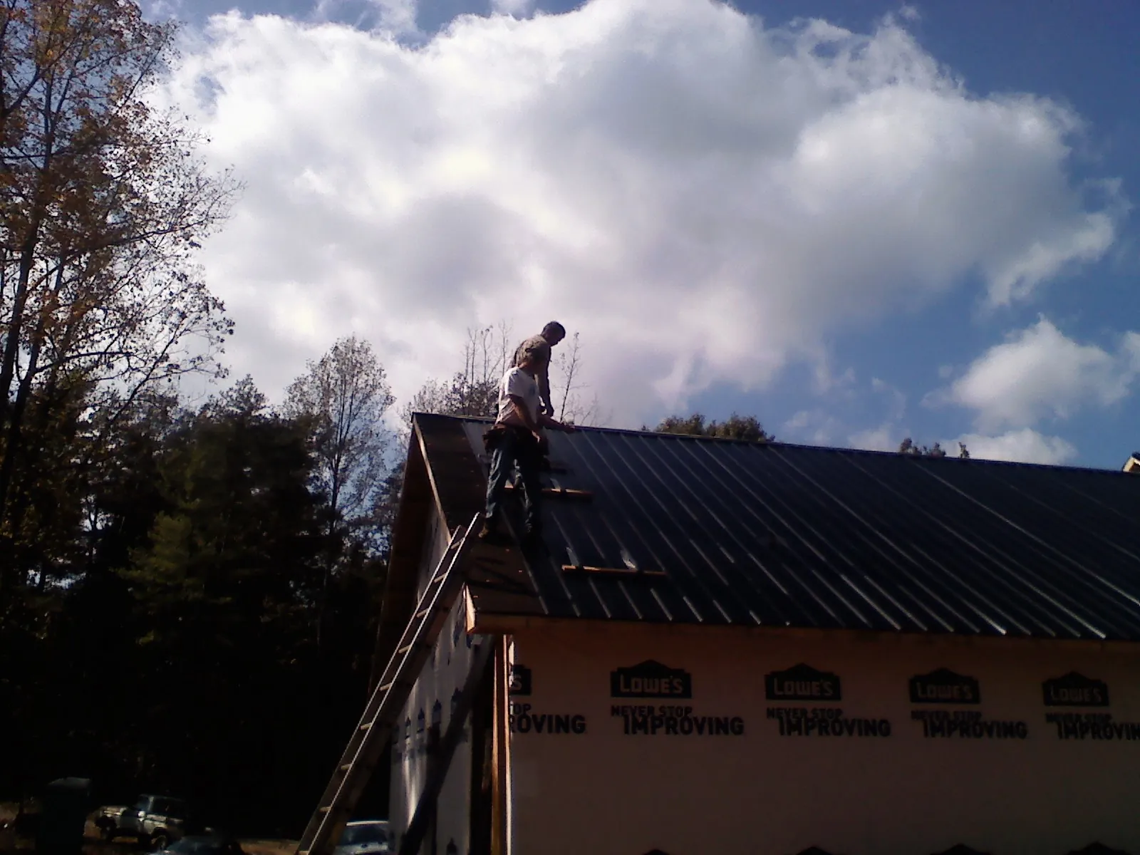 Roofer fastening dark metal panels high against a cloudy sky, from a Roof Inspection job in Quakertown