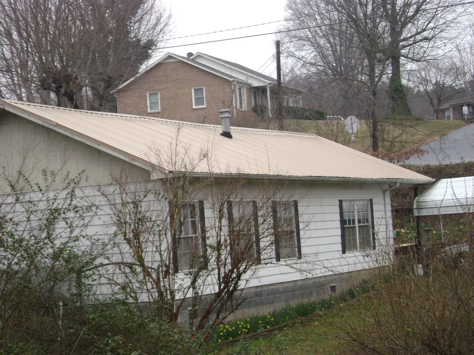 Tan metal roof on a white sided house set into a hillside — Commercial Roofing by Roofing Brothers in Quakertown