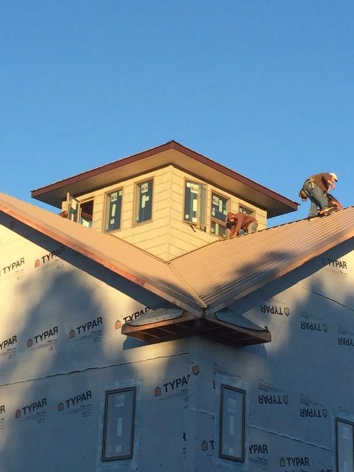 Roofers working around a rooftop cupola on a new metal roof at sunset in Quakertown
